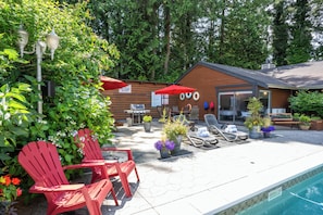A poolside area with red Adirondack chairs, a barbecue grill, and a wooden building with a sign that reads 'POO'.