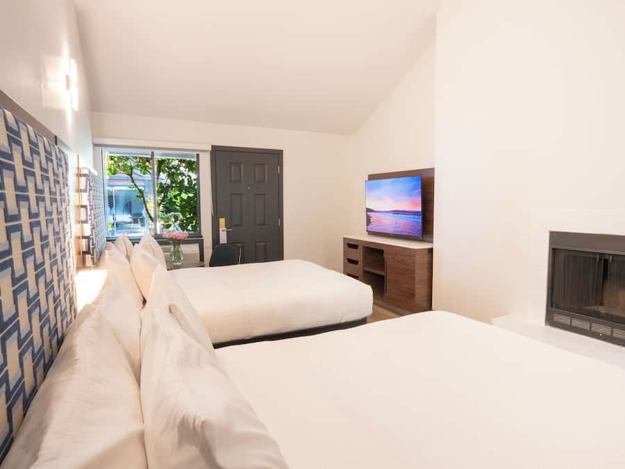 Ein Hotelzimmer mit zwei Betten, einem Fernseher, einem Kamin und Blick auf einen Garten und eine Außenanlage.