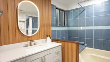 A bathroom with a wooden vanity, a white sink, a mirror with a light, and a blue-tiled shower area.