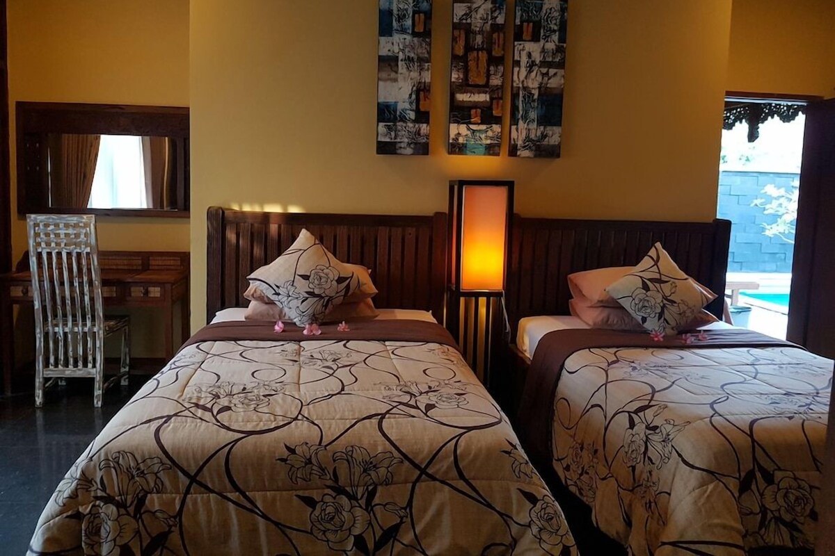 Habitación de hotel con dos camas, una mesita de noche, una lámpara y cuadros en la pared.