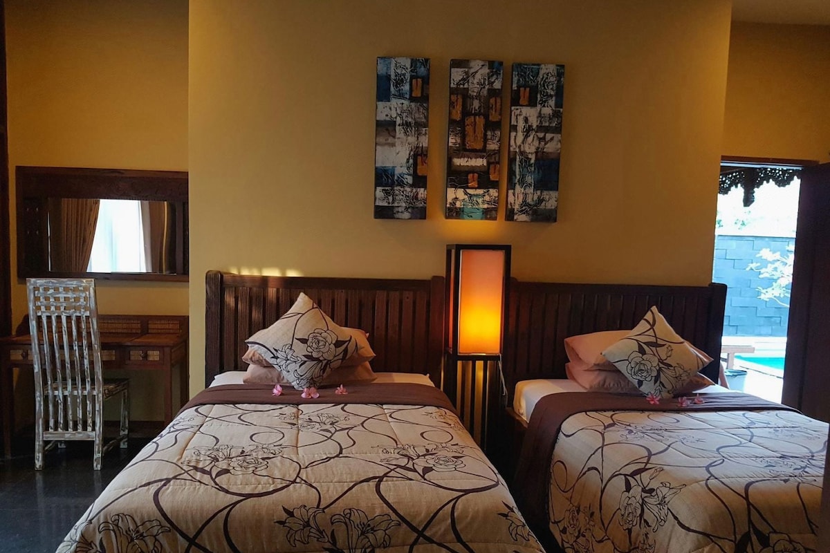 Habitación de hotel con dos camas, una mesita de noche, una lámpara y una obra de arte en la pared.