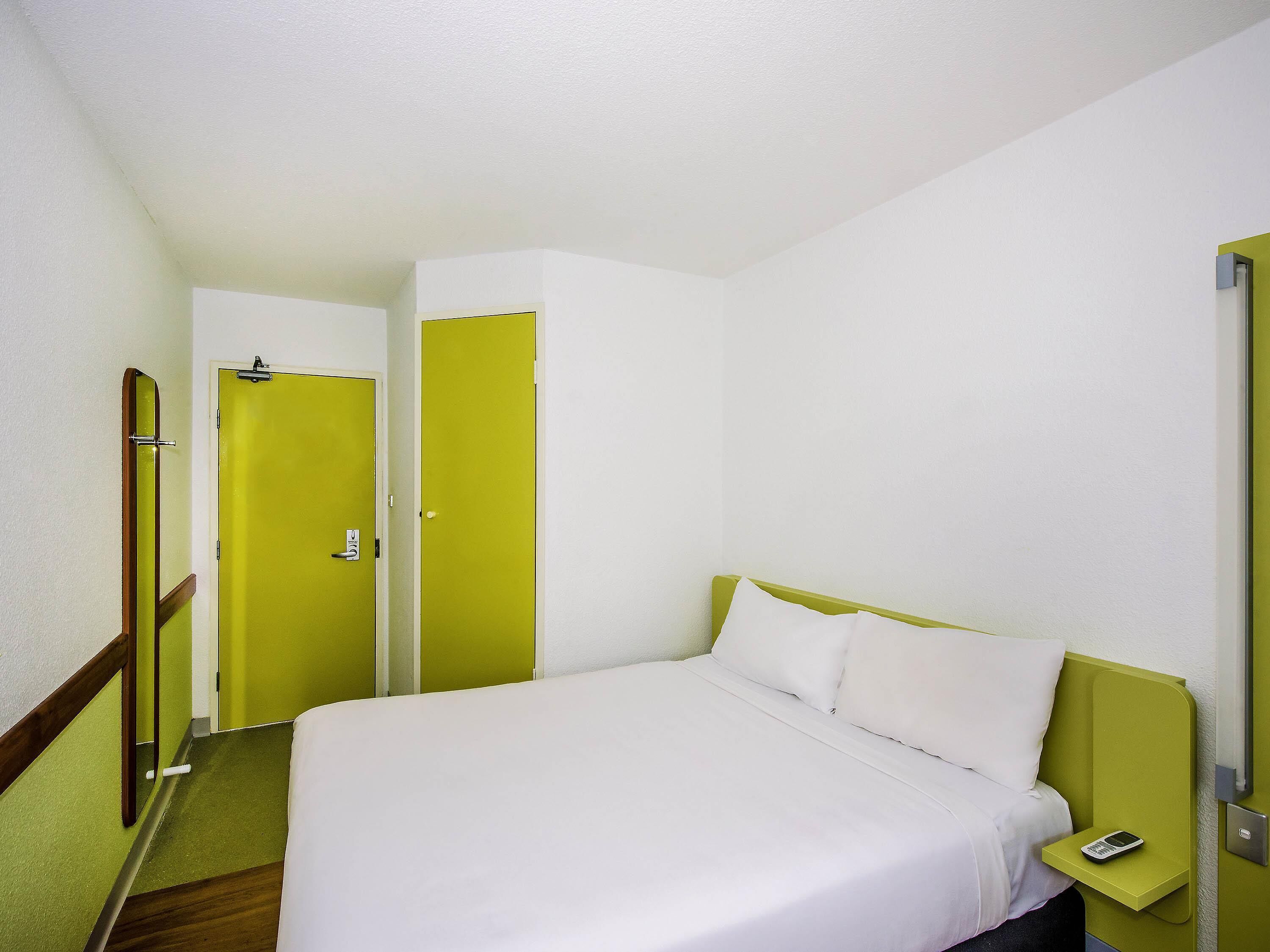 A single bed with white bedding, a bedside table with a phone, and a green wall.