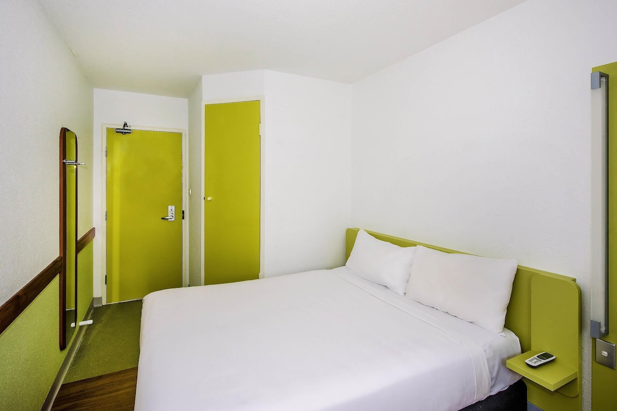 A single bed with white bedding, a bedside table with a phone, and a green wall.