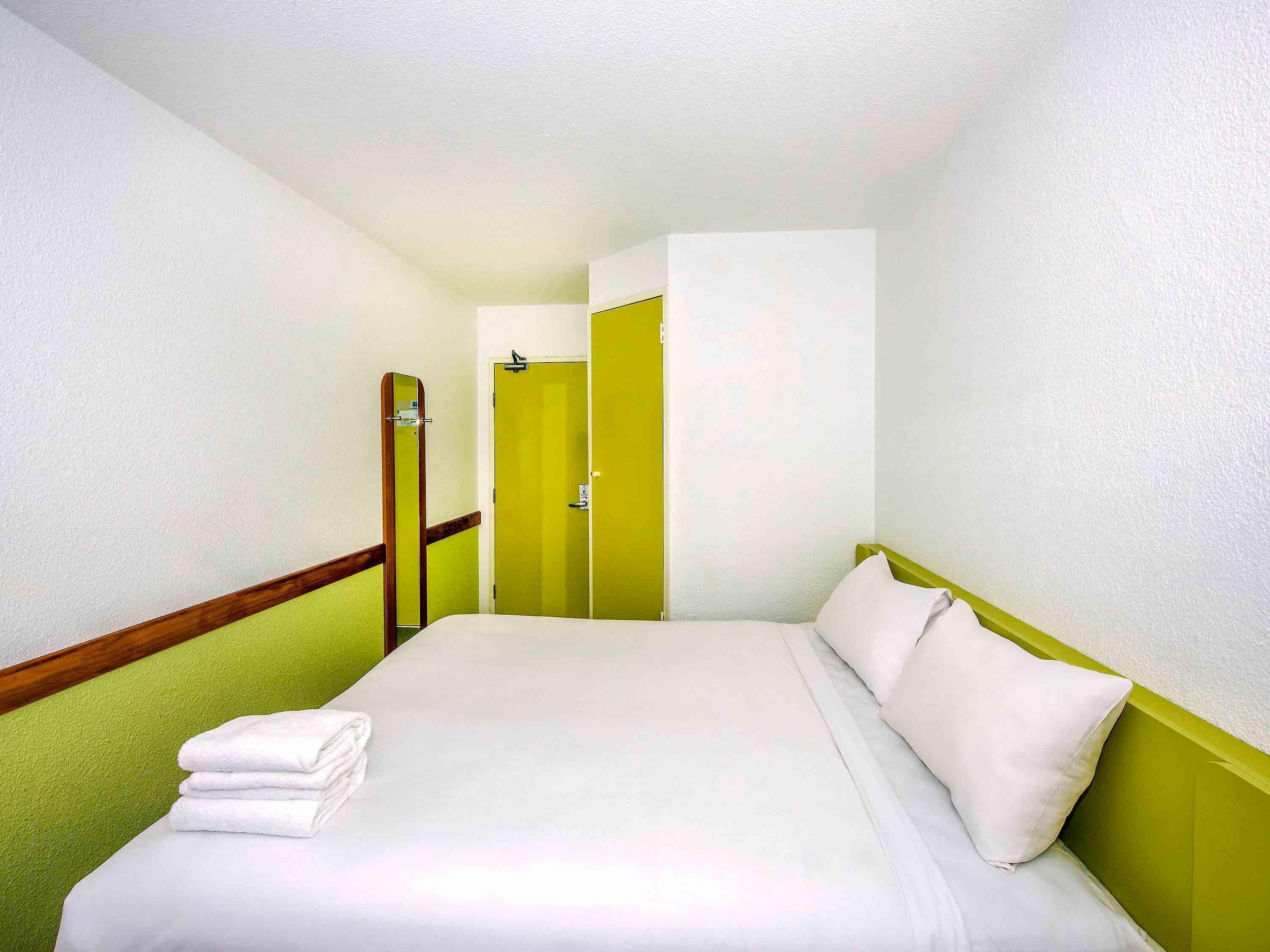 A hotel room with a bed, a green wall, and a door.