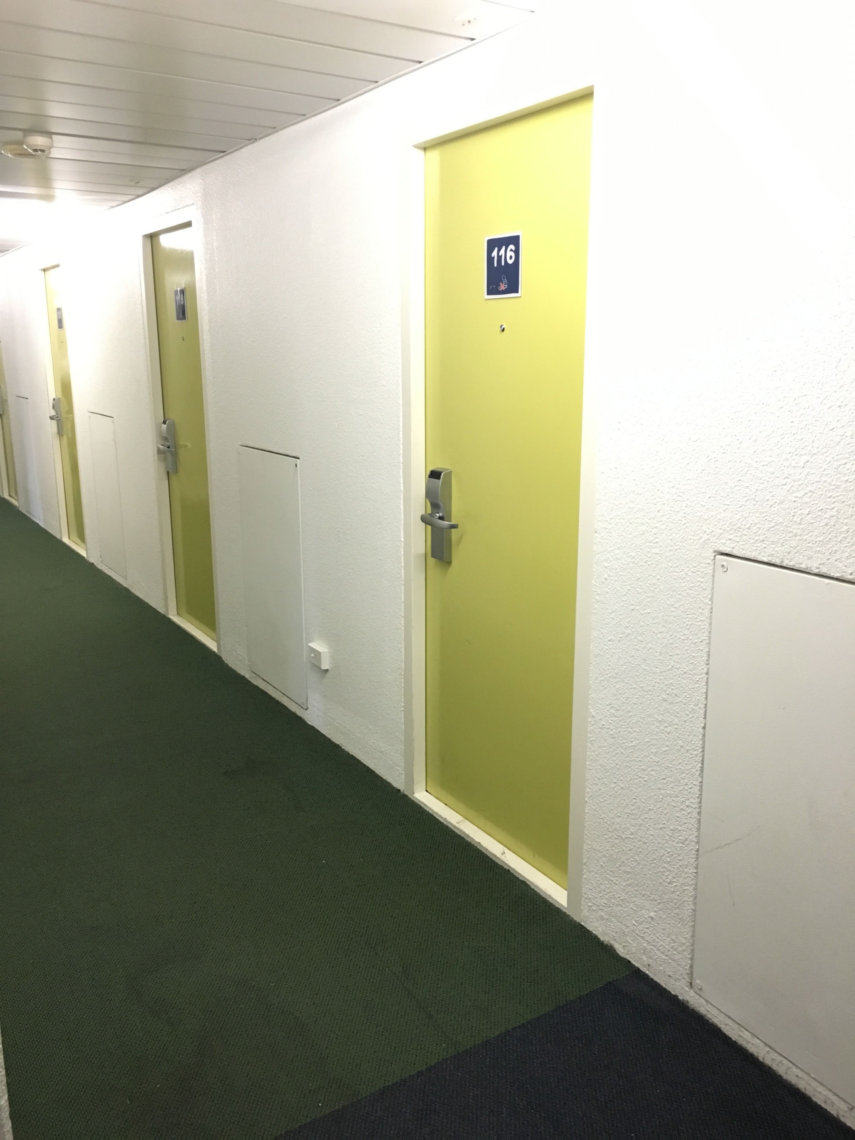 Un pasillo con puertas numeradas 116, 117 y 118, que conducen a habitaciones de hotel.
