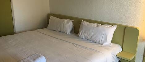 A neatly made bed with white linens and pillows, a green headboard, and a bedside table with a light-colored nightstand.