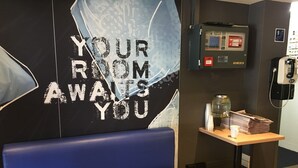 Un área de espera con un banco azul, una pared con un mensaje, una mesita con dispensador de agua y un teléfono.