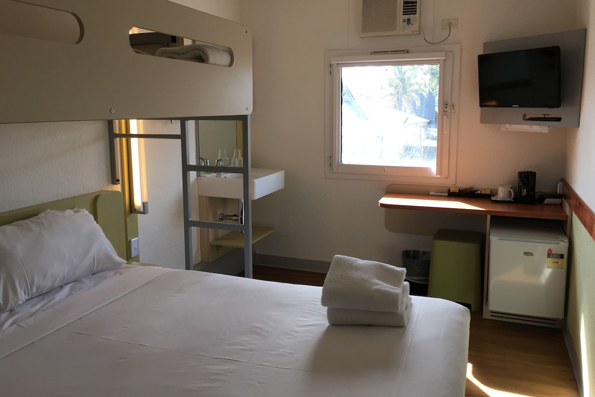 Une chambre d’hôtel comprenant un lit, un bureau avec une télévision, une fenêtre et un petit réfrigérateur.