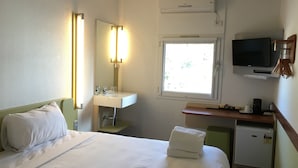A hotel room with a bed, a sink, a mirror, a TV, and a window. - Ibis Budget St Peters (St Peters)