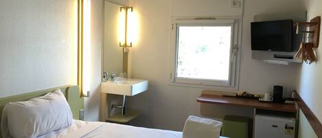 Habitación de hotel con cama, lavamanos, espejo, televisión y ventana.
