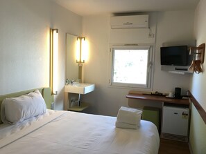 A hotel room with a bed, a sink, a mirror, a TV, and a window. - Ibis Budget St Peters (St Peters)
