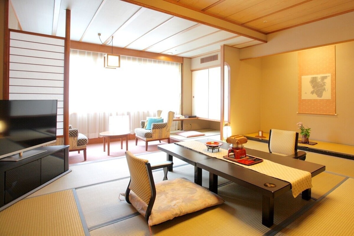 A traditional Japanese room with tatami flooring, a low table with a red tray, a television, and a sliding door leading to another room.