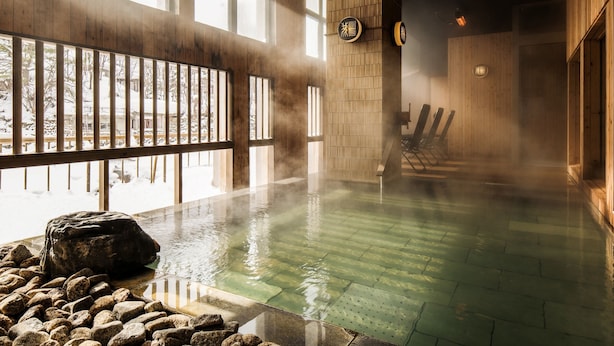 A hot spring bath with wooden walls, large windows, and a stone seating area. - Hotel Shikanoyu (Sapporo)