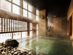 A hot spring bath with wooden walls, large windows, and a stone seating area. - Hotel Shikanoyu (Sapporo)