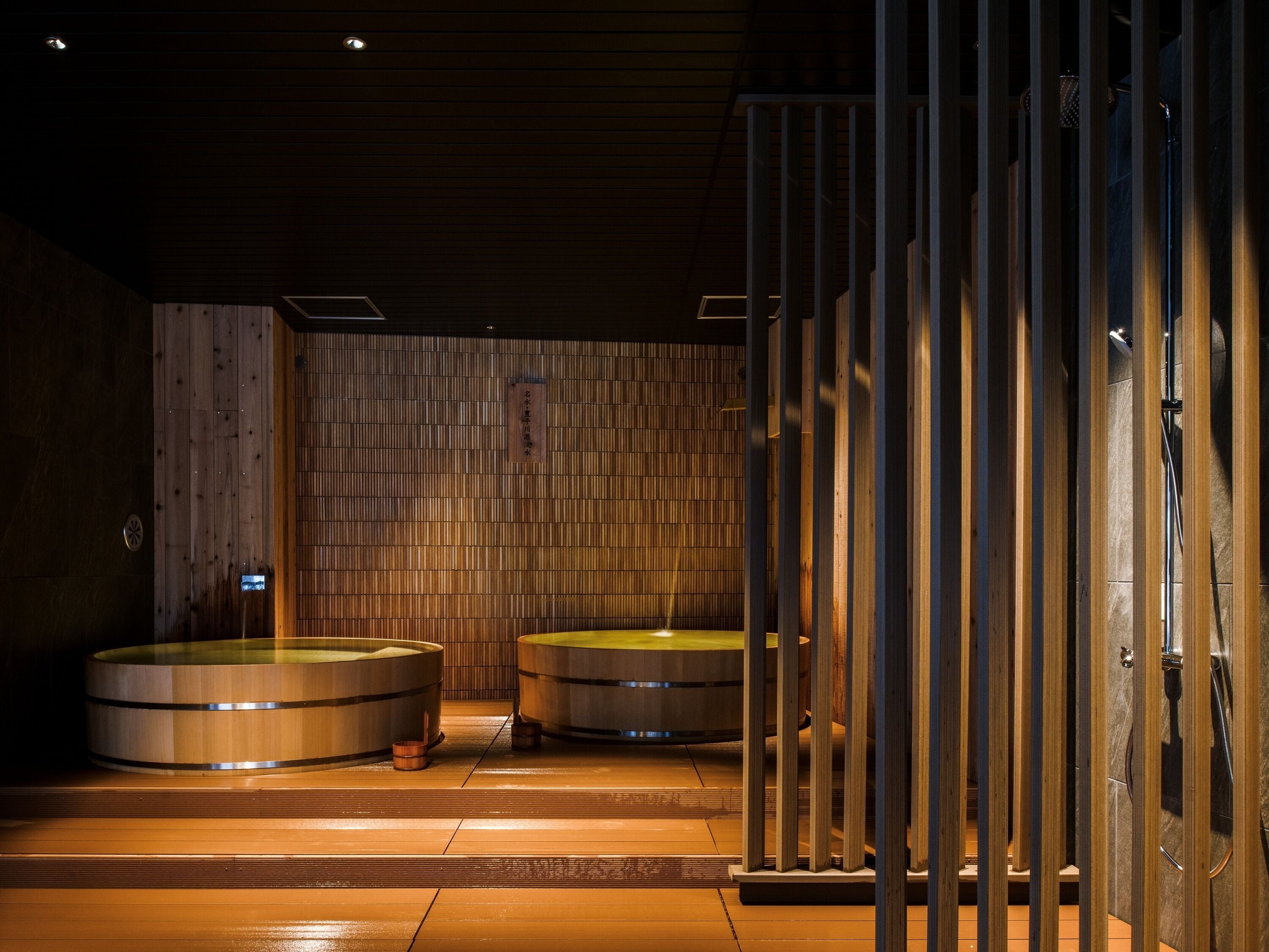 A traditional Japanese onsen with wooden walls and two hot tubs.