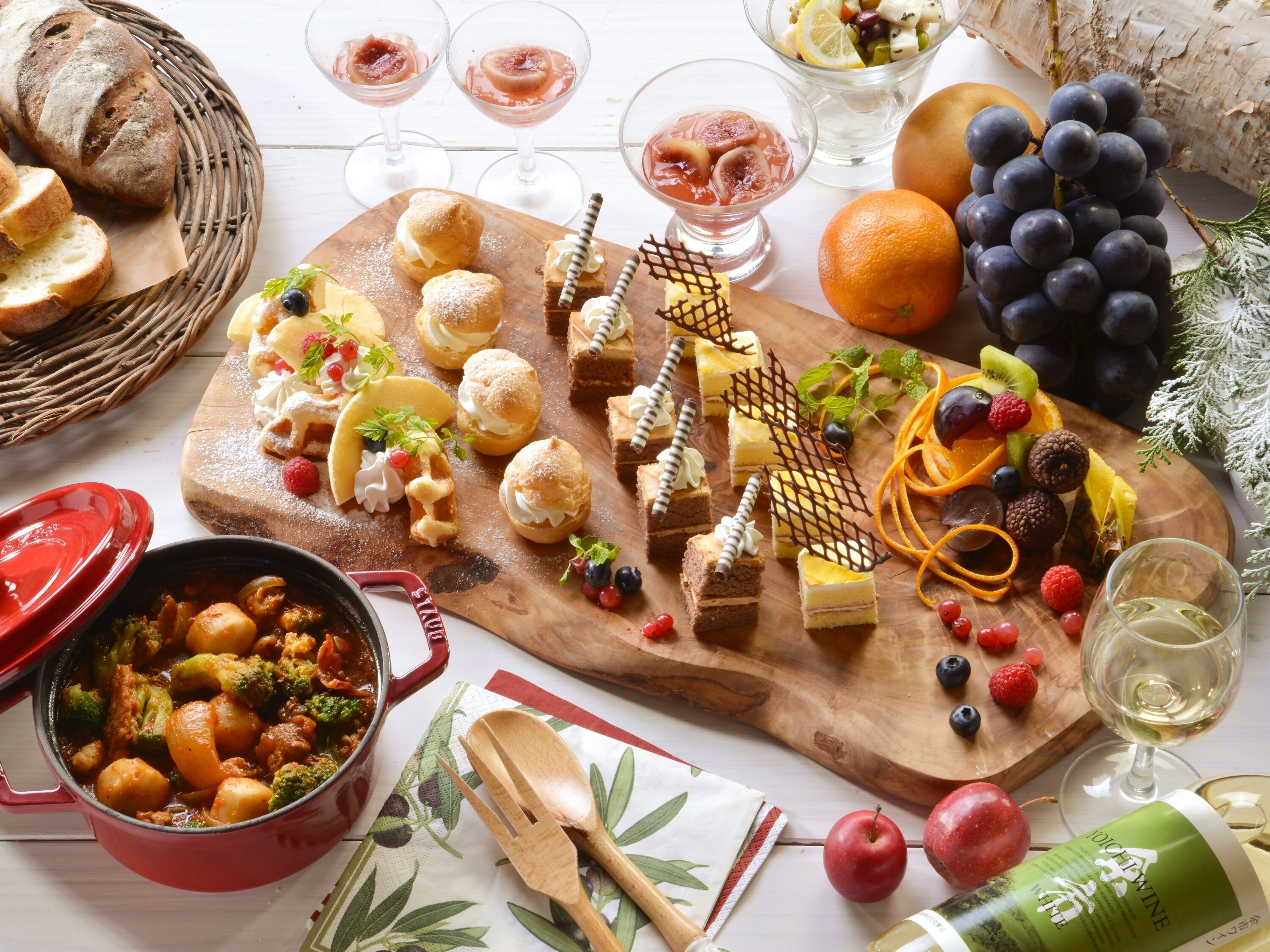 Una tabla de madera con diversos pasteles, frutas y una olla de guiso.