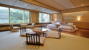 A traditional Japanese-style room with tatami flooring, a low bed, a sofa, and a dining table with chairs. - Hotel Shikanoyu (Sapporo)
