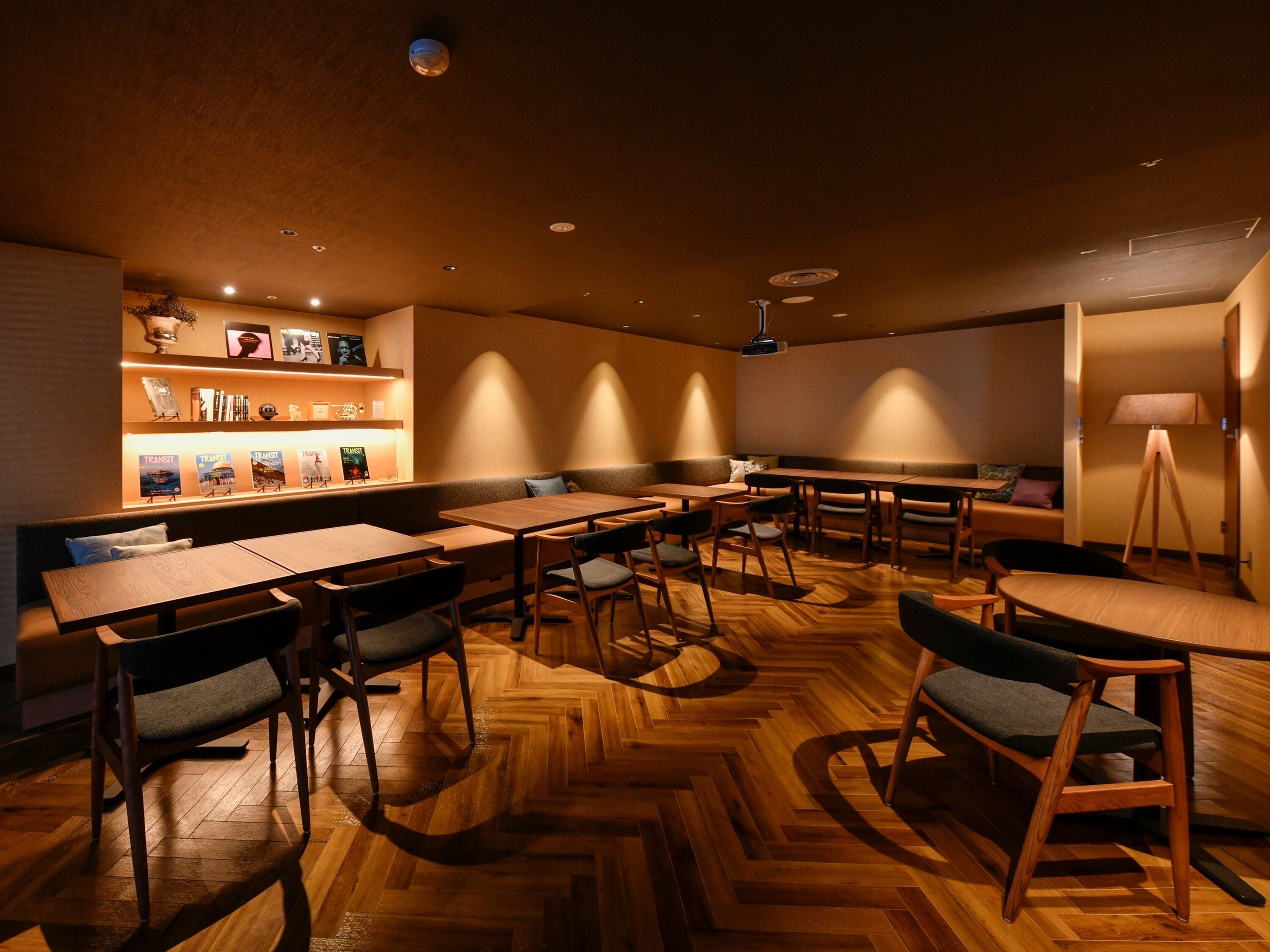 A modern interior with wooden flooring, multiple seating arrangements, and a wall-mounted shelf with books.
