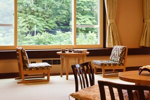 Una habitación con un ventanal grande, dos sillas, una mesita y una mesa de madera.