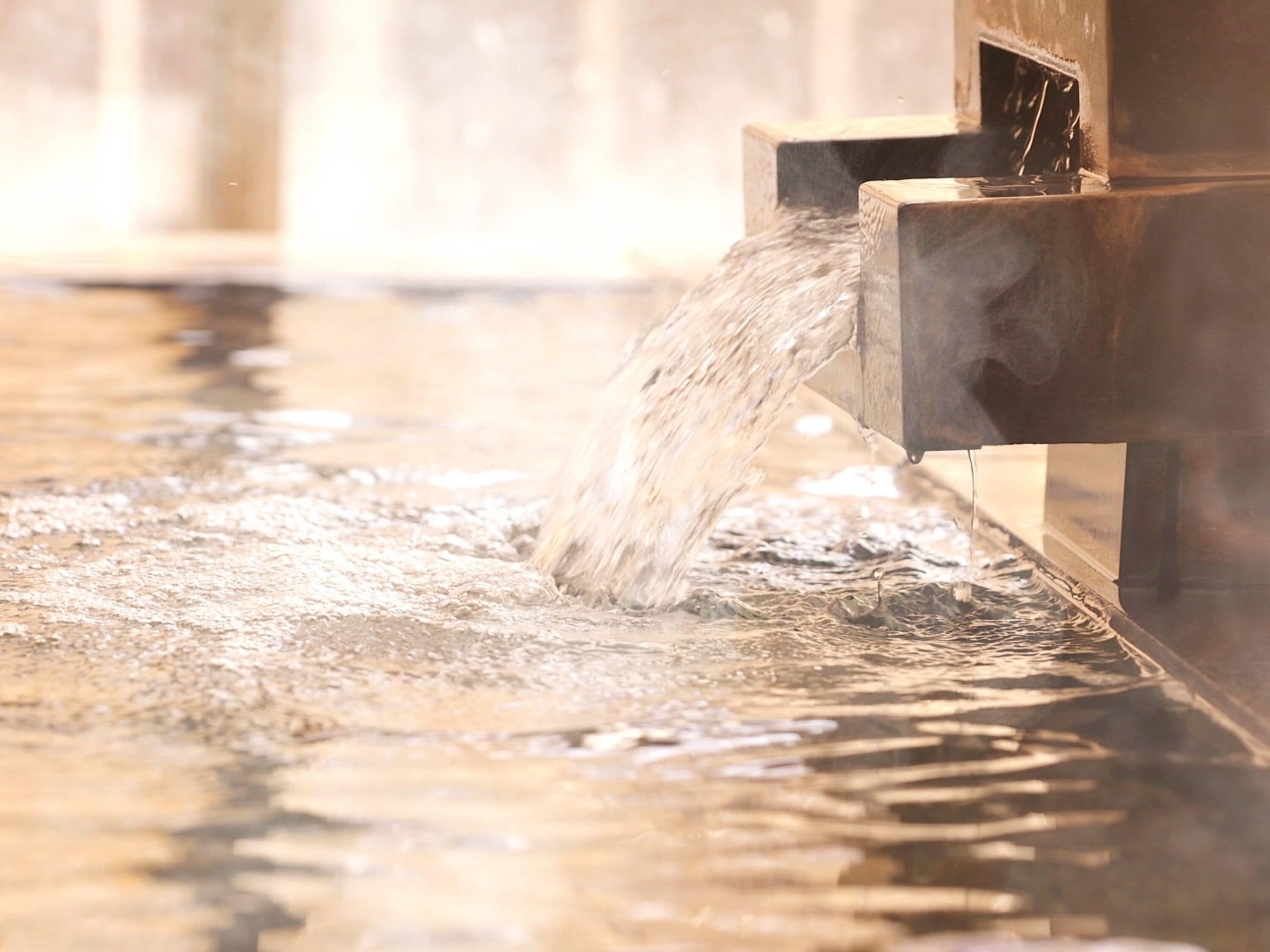 Water flowing from a metal spout into a shallow pool.