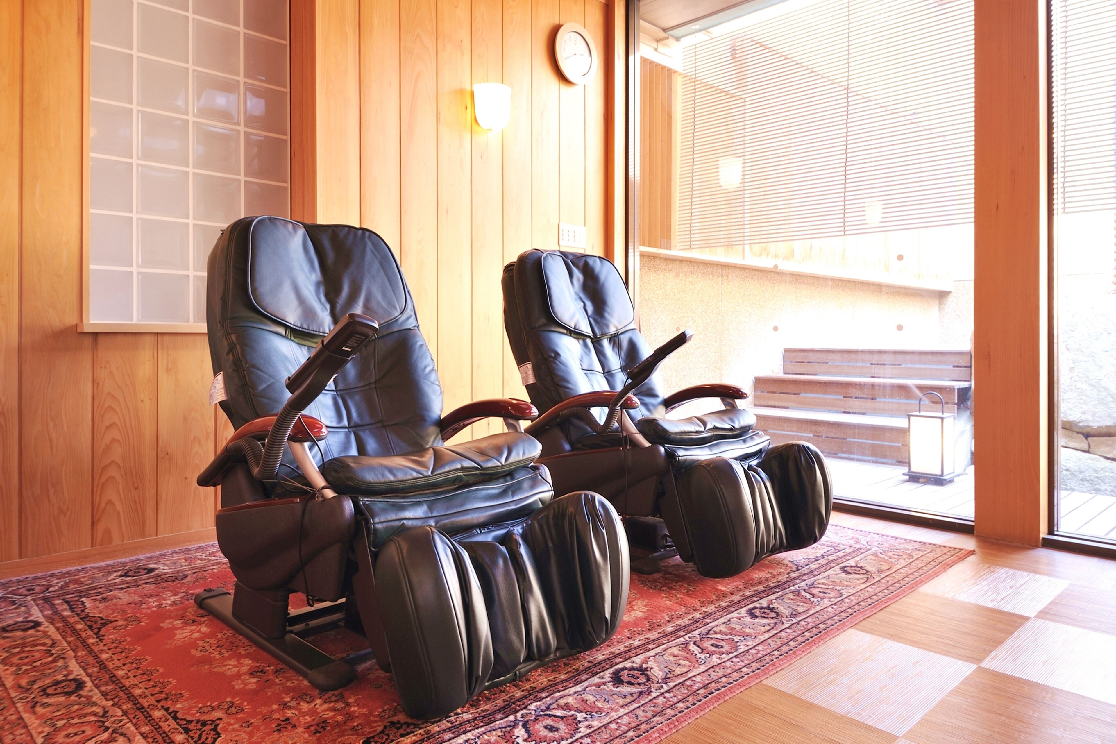 Two massage chairs in a room with wooden walls and a large window.