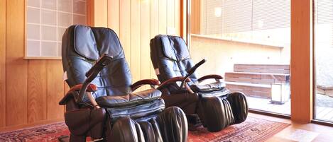 Two massage chairs in a room with wooden walls and a large window.