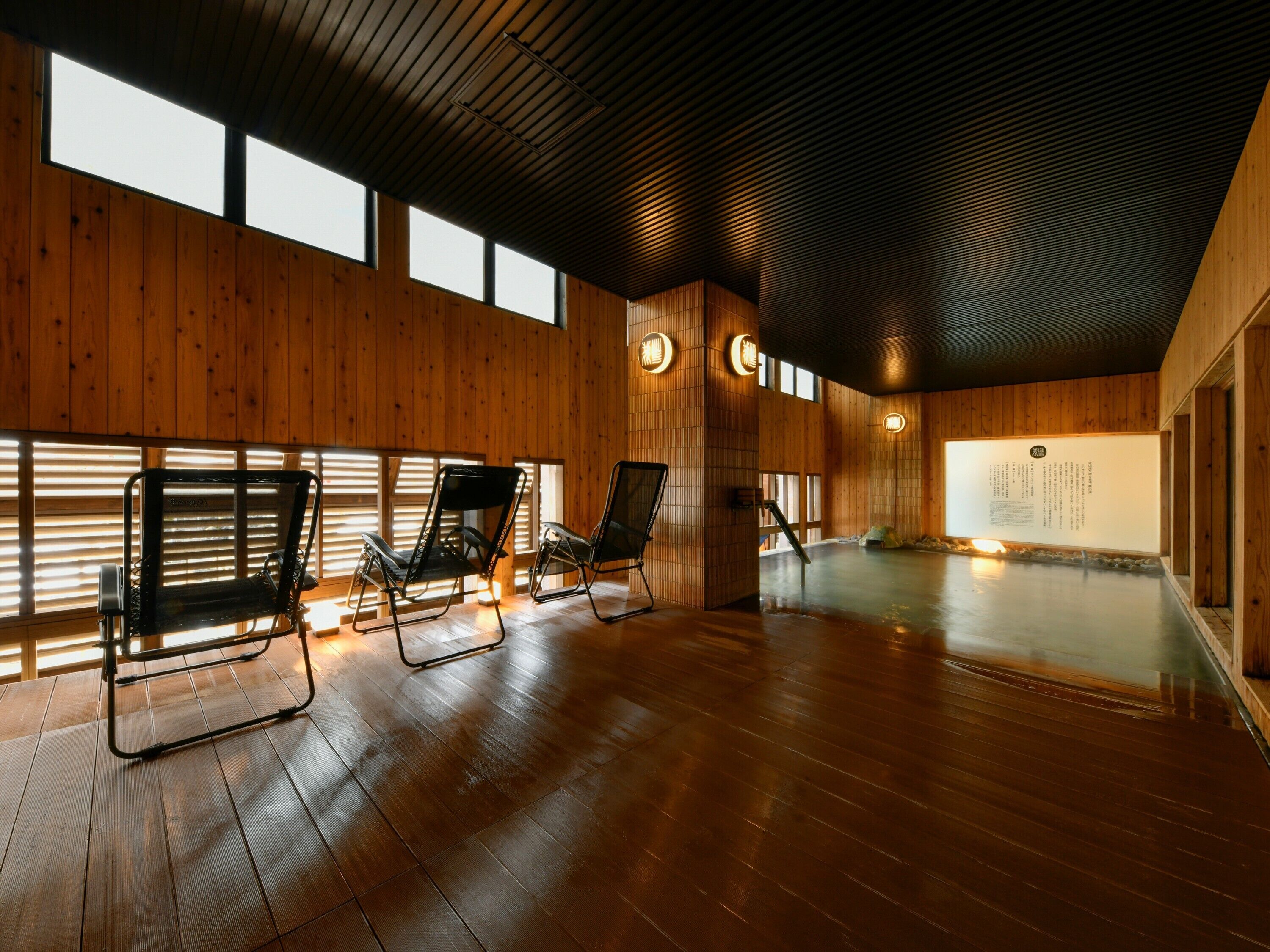 A spacious room with wooden walls and a high ceiling, featuring three black chairs and a large wall-mounted screen.