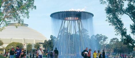 A public park with a large fountain in the center, surrounded by trees and a crowd of people.