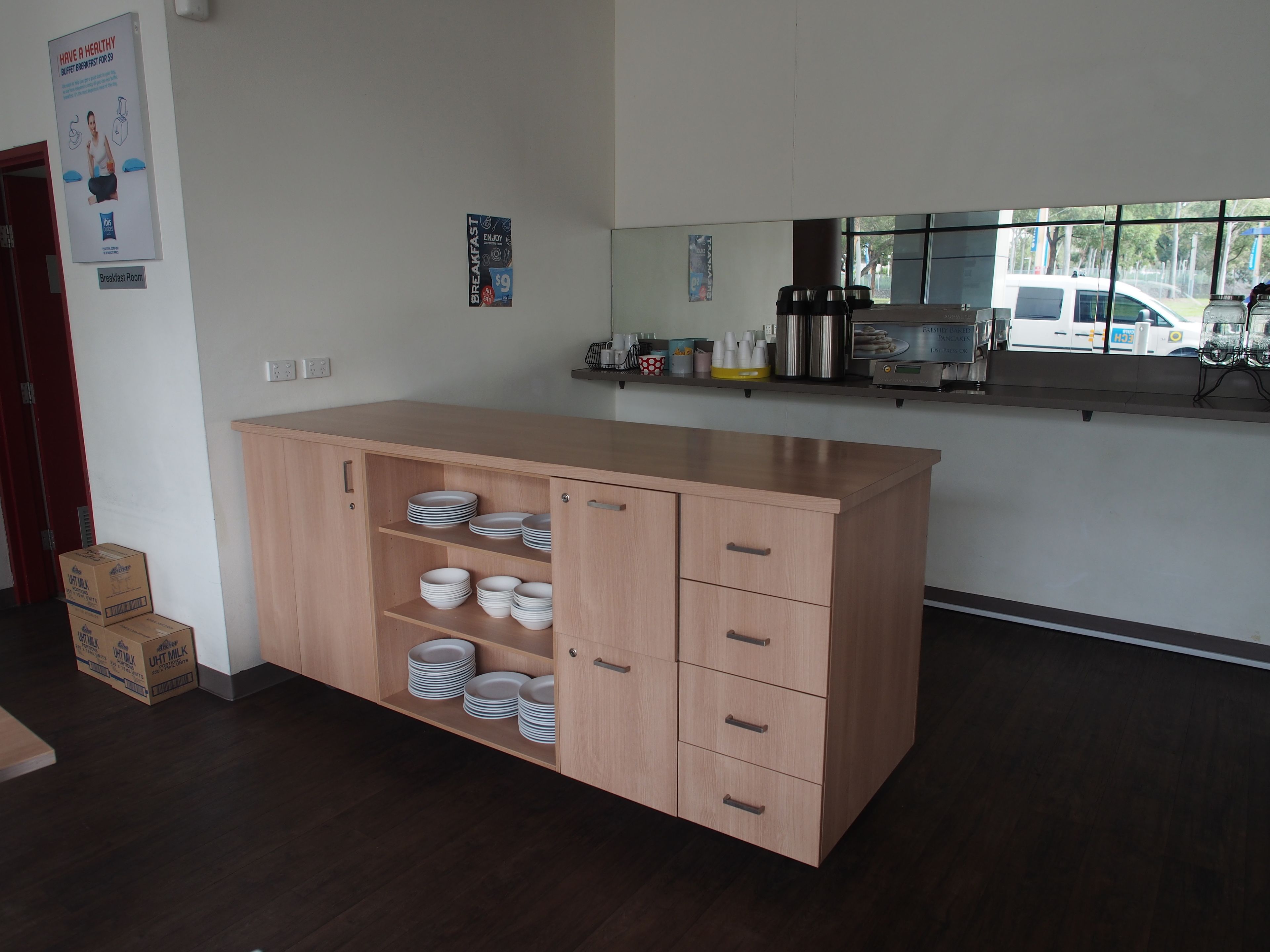 Una cocina moderna con un armario de madera, platos blancos y un cartel de desayuno en la pared.