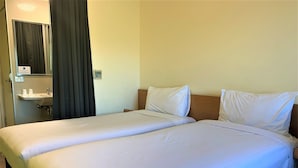 Een hotelkamer met twee eenpersoonsbedden, een badkamer met wastafel en spiegel, en een gordijn.