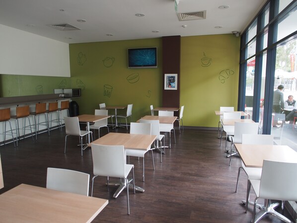 Un café moderno con una pared verde, sillas blancas y mesas de madera.