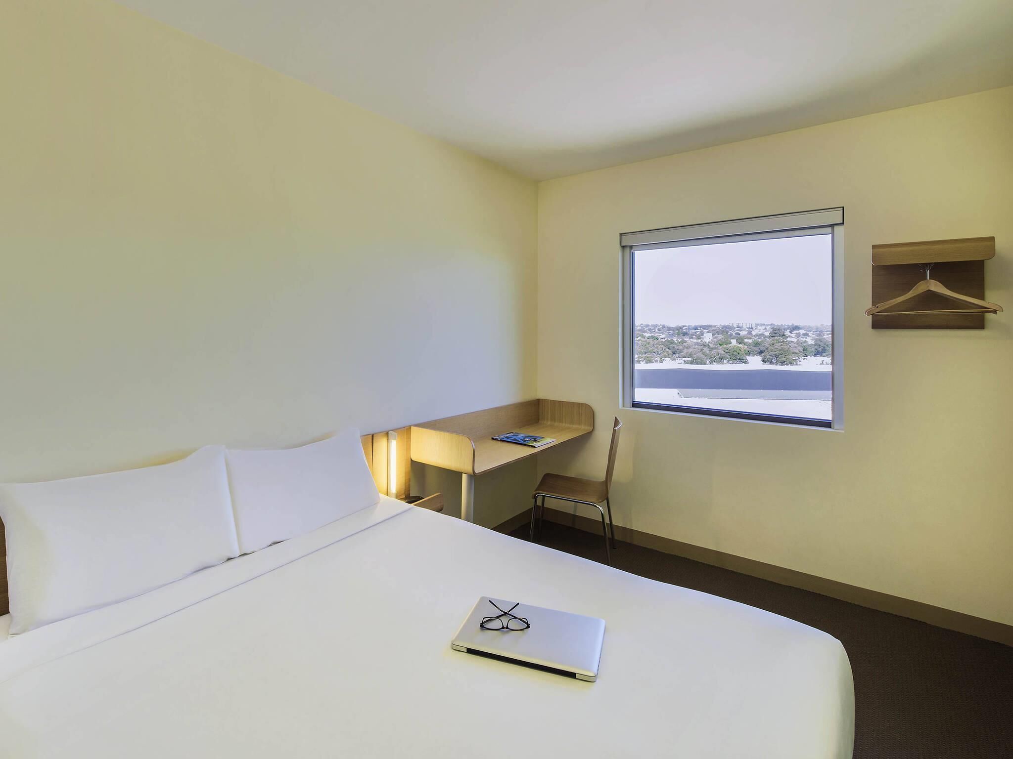 Une chambre d’hôtel équipée d’un lit, d’un bureau, d’une chaise, d’une fenêtre donnant sur un paysage agréable et d’un porte-manteau.