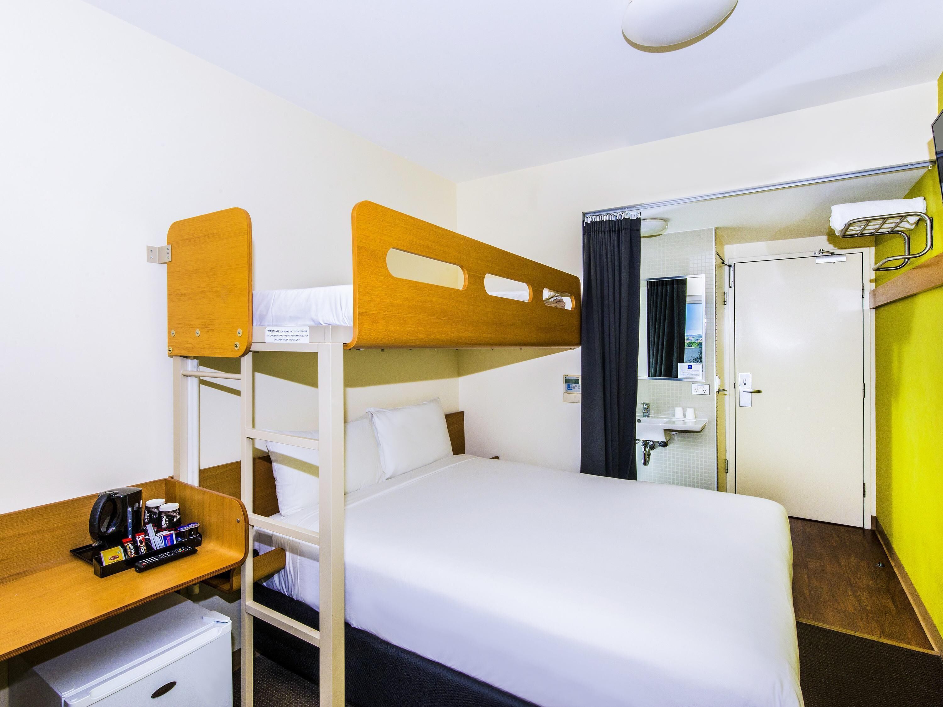A bunk bed room with a desk, a mini fridge, and a bathroom visible through a door.