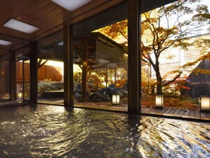 A modern interior with a glass wall, wooden flooring, and a view of an outdoor garden with autumn foliage. - Hanamomiji (Sapporo)