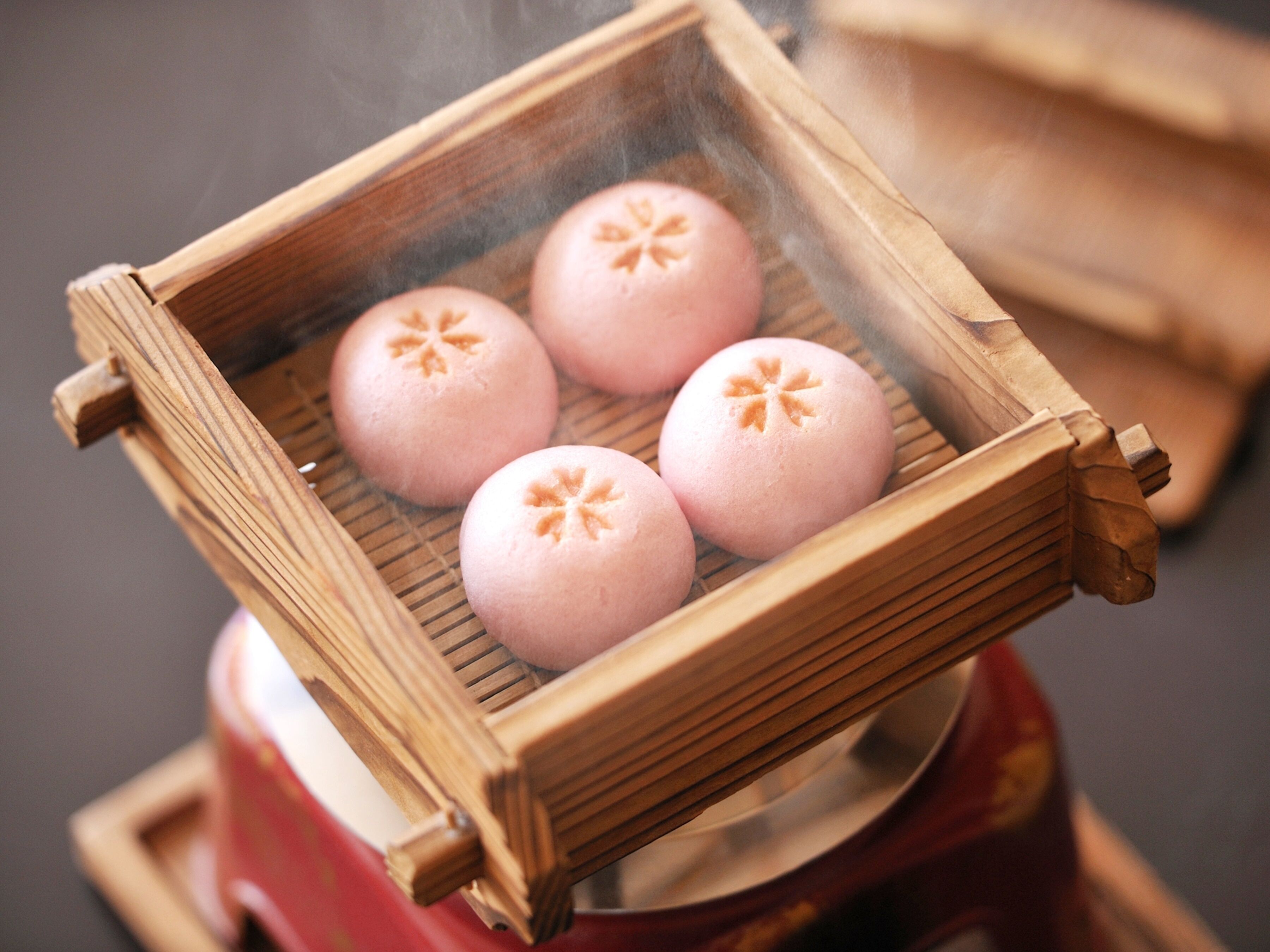 A traditional bamboo steamer with four round, pink steamed buns.
