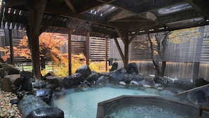 Un onsen japonés tradicional con un balneario de madera, rocas y una terraza de madera.