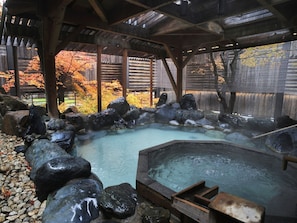 A traditional Japanese onsen with a wooden bath, rocks, and a wooden deck. - Hanamomiji (Sapporo)