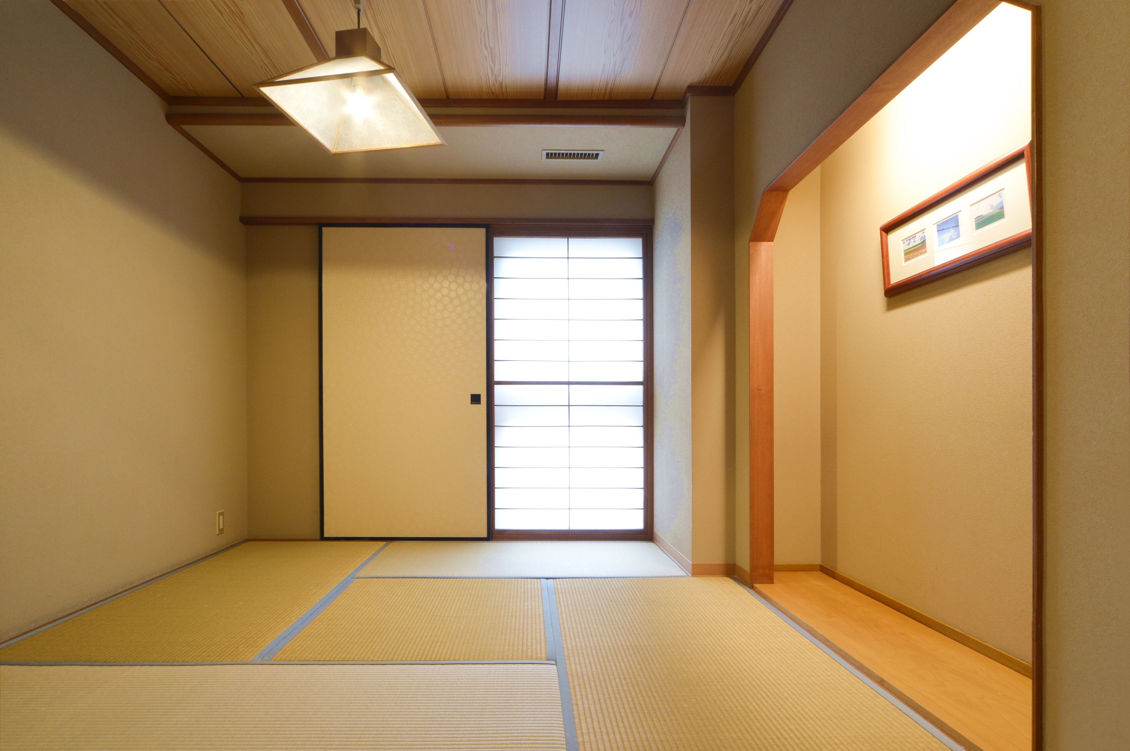 A traditional Japanese room with tatami flooring, a sliding door, and a ceiling light fixture.