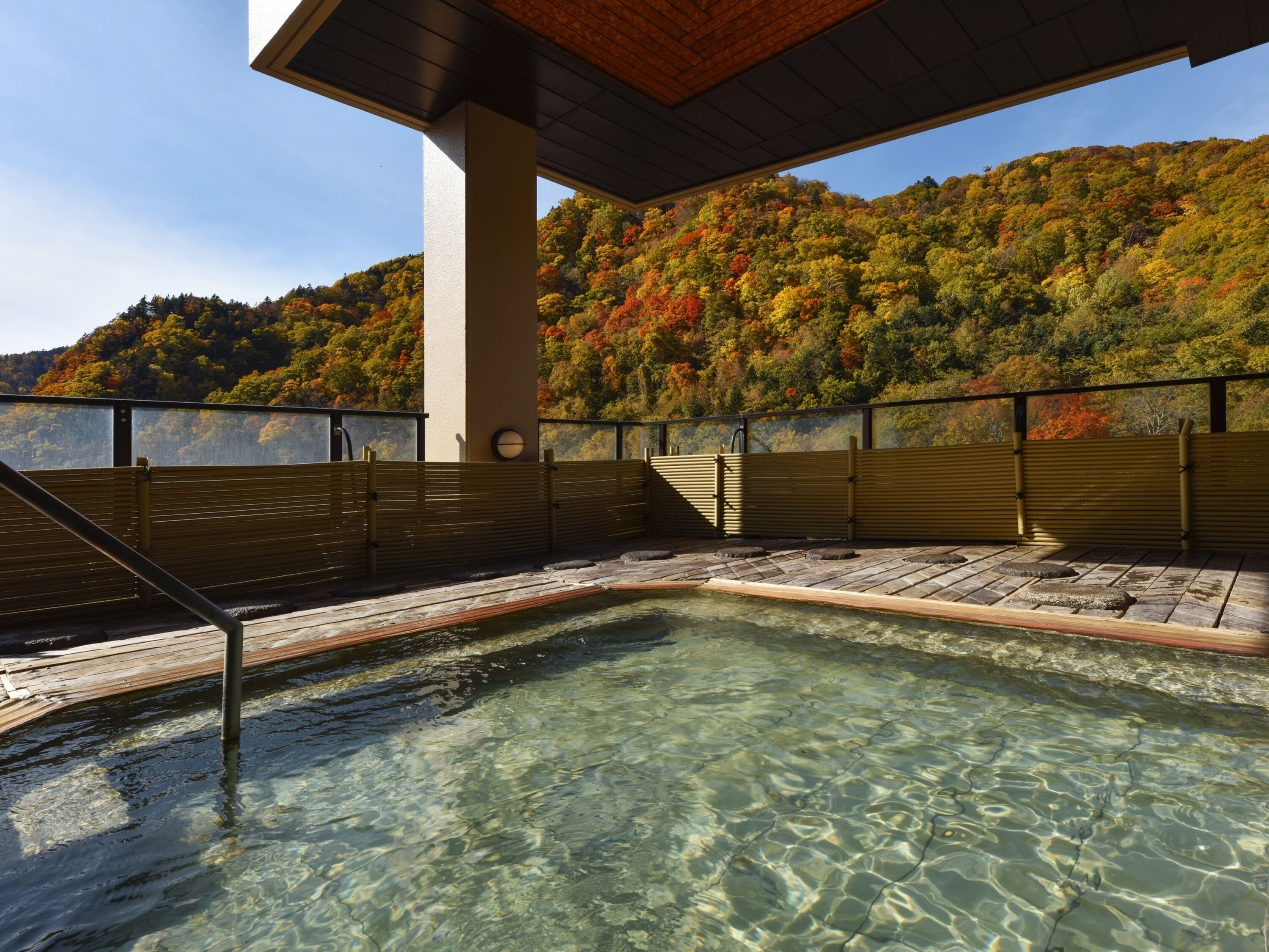 A hot spring area with clear water, wooden benches, and a view of a forested hillside.