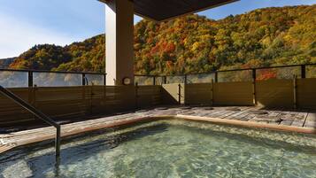 A hot spring area with clear water, wooden benches, and a view of a forested hillside.
