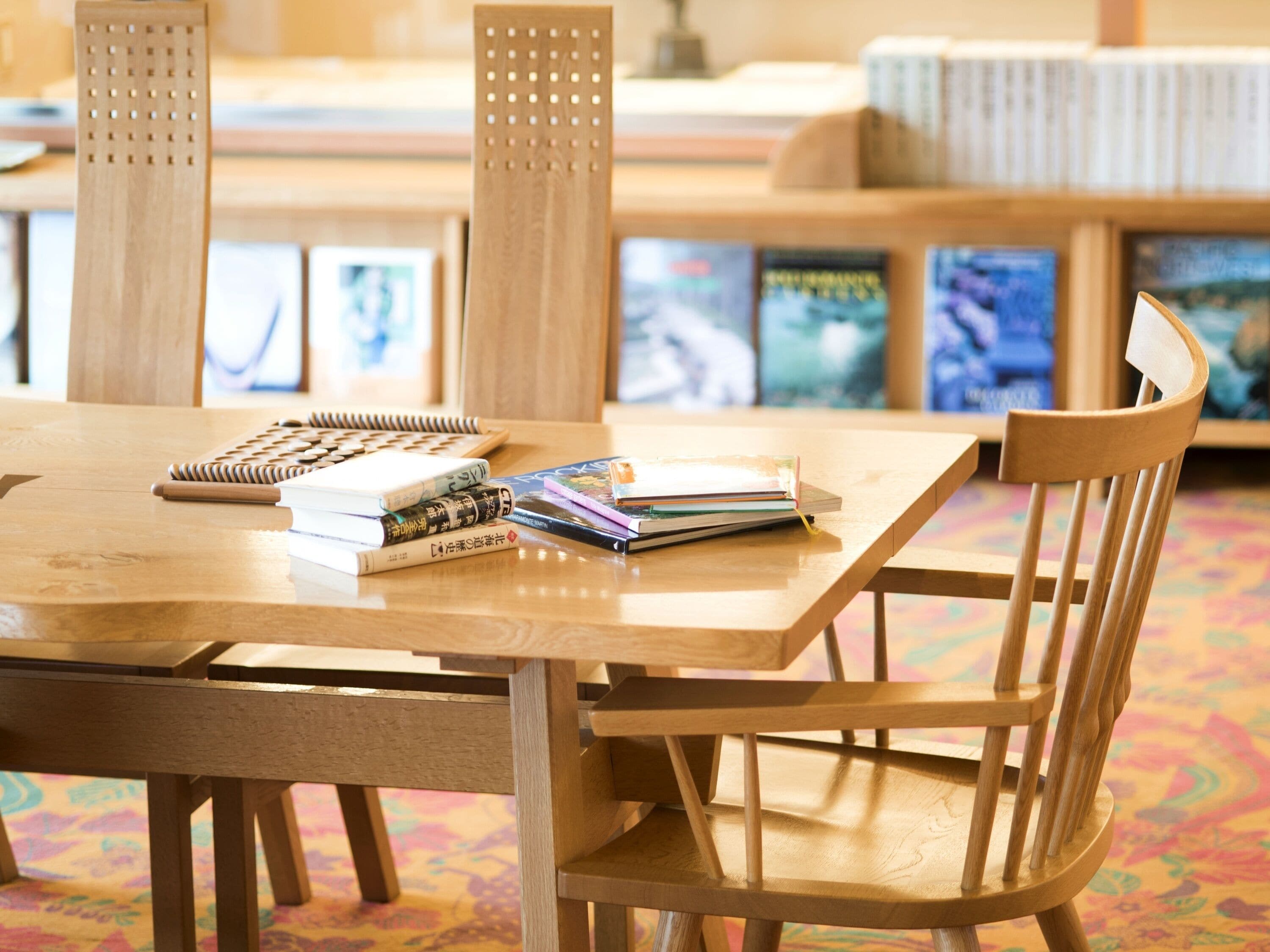 A wooden table with books and a notebook, surrounded by wooden chairs in a room with a patterned floor.