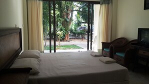 A hotel room with a bed, a television, and a view of a garden through a sliding door. - Jinta City Samui (Koh Samui)