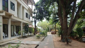 A courtyard with a pathway, trees, and a building with a balcony. - Jinta City Samui (Koh Samui)