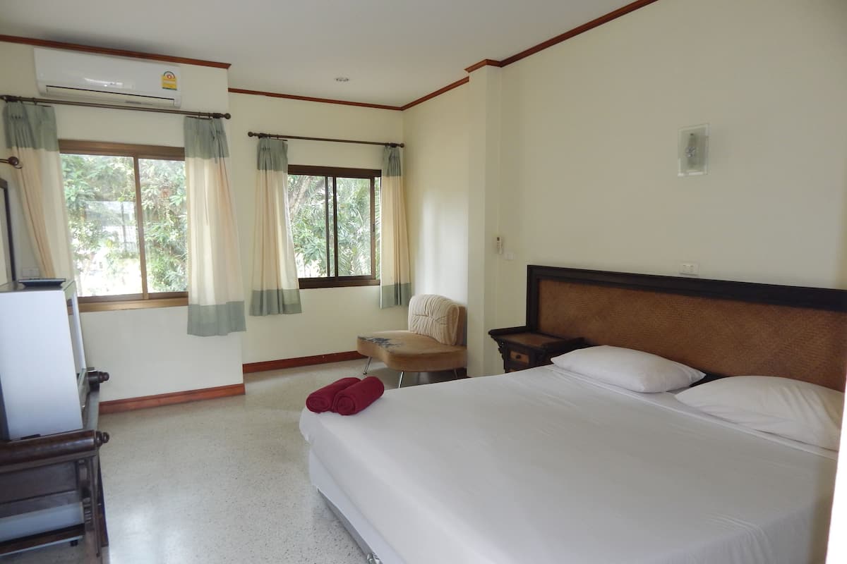 A hotel room with a bed, a chair, a desk, and a window with curtains.