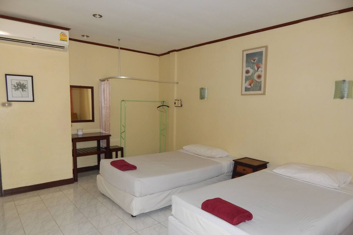 A hotel room with two single beds, a desk, a chair, a mirror, and a green metal drying rack.