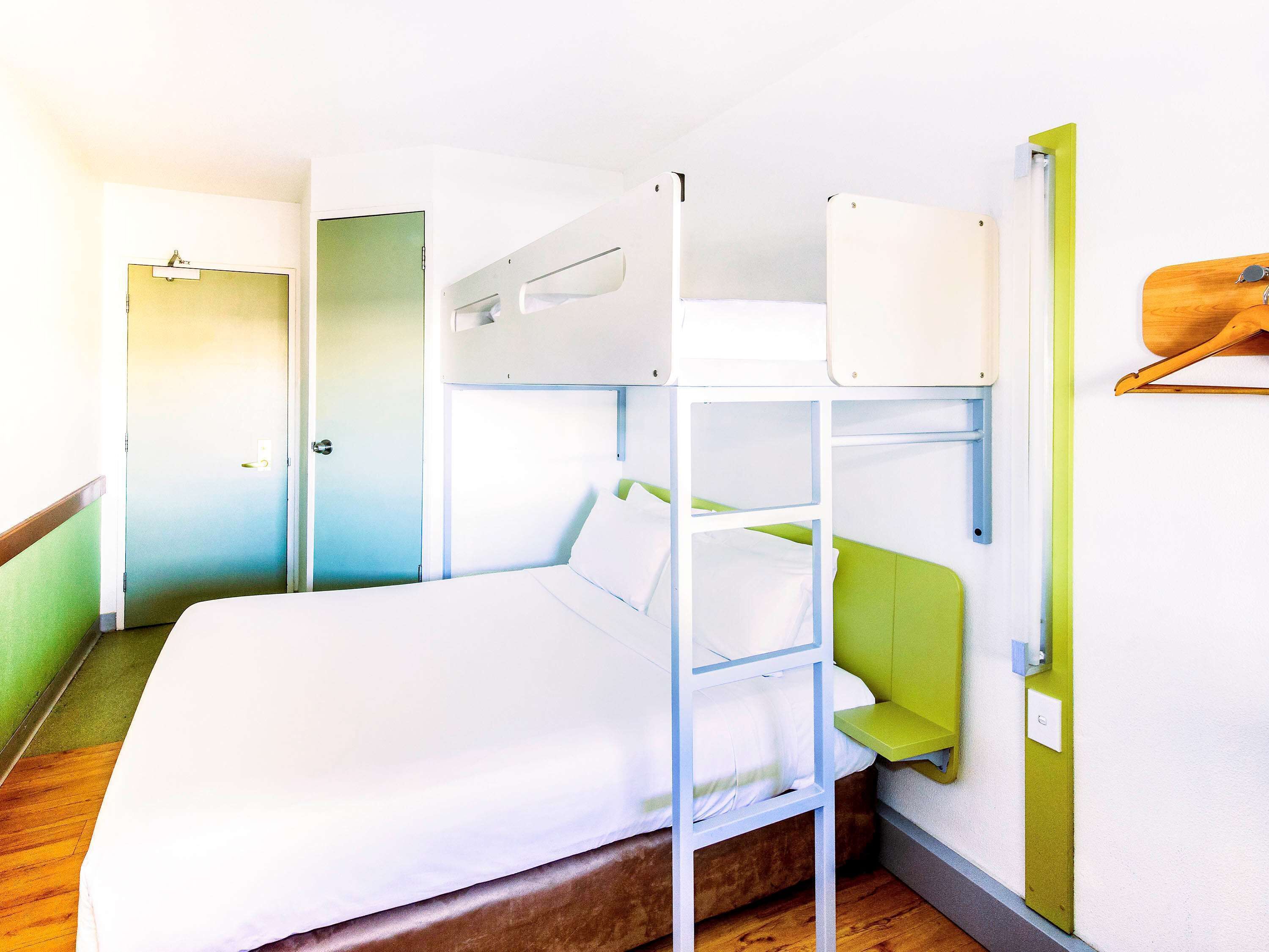Una cama litera con cabecera verde y ropa de cama blanca en una habitación con piso de madera y pared verde.