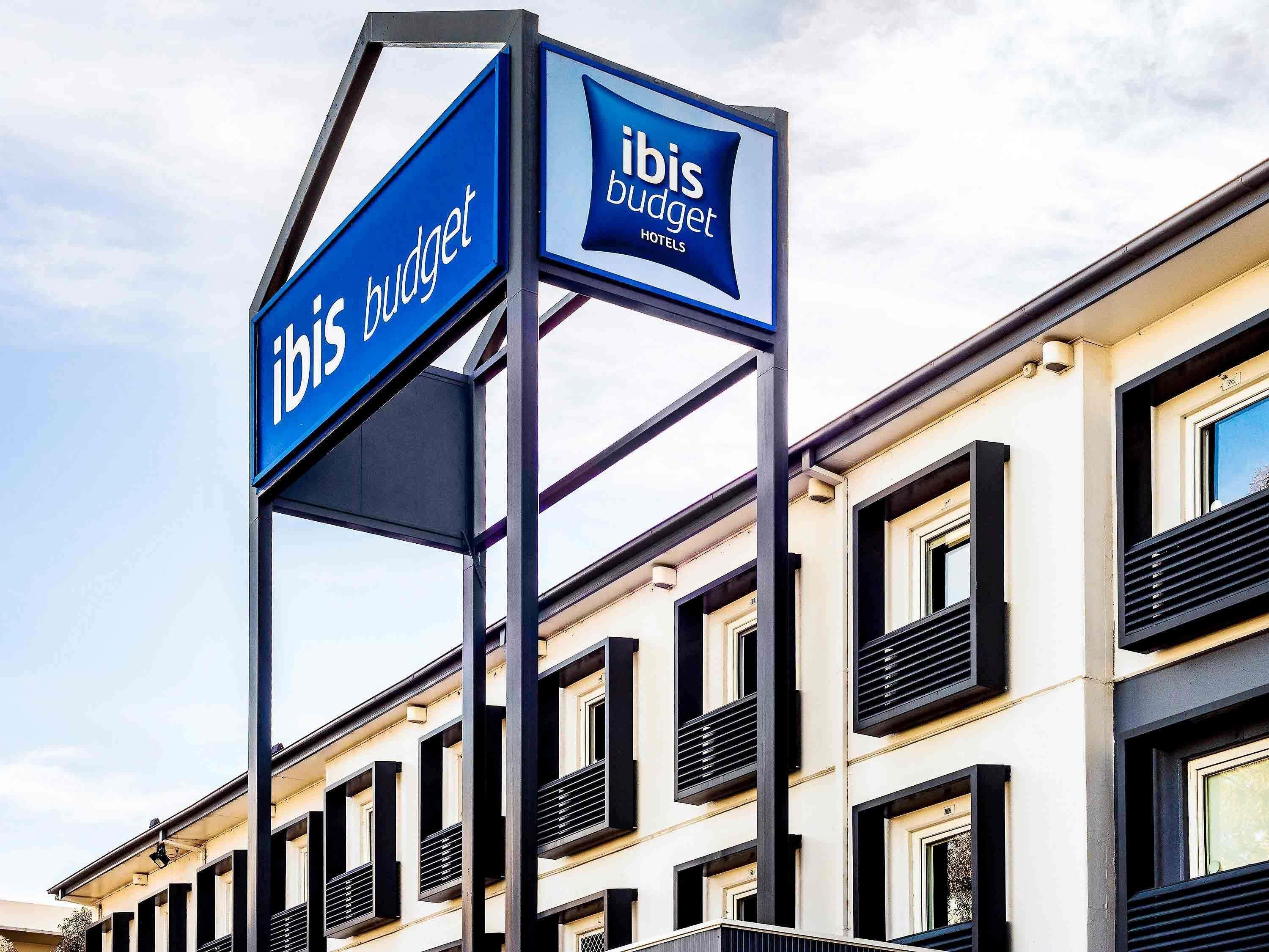 Ein Schild für Ibis Budget Hotels mit einem modernen Gebäude im Hintergrund.