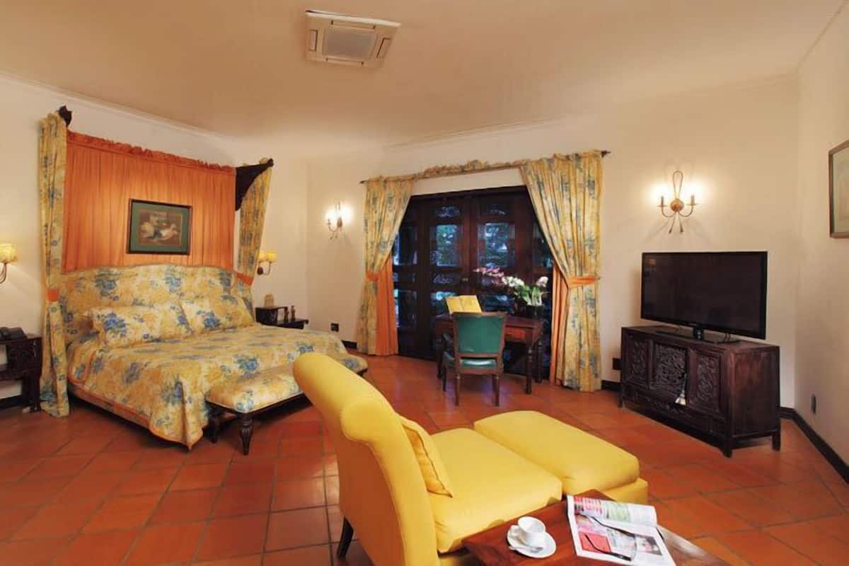 Una habitación de hotel con cama, un sillón amarillo, un televisor y vistas al exterior.