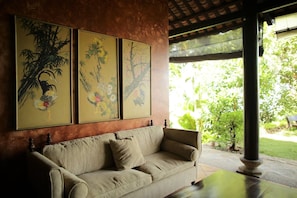 A beige sofa with a cushion, a wooden table, and three framed paintings on the wall.