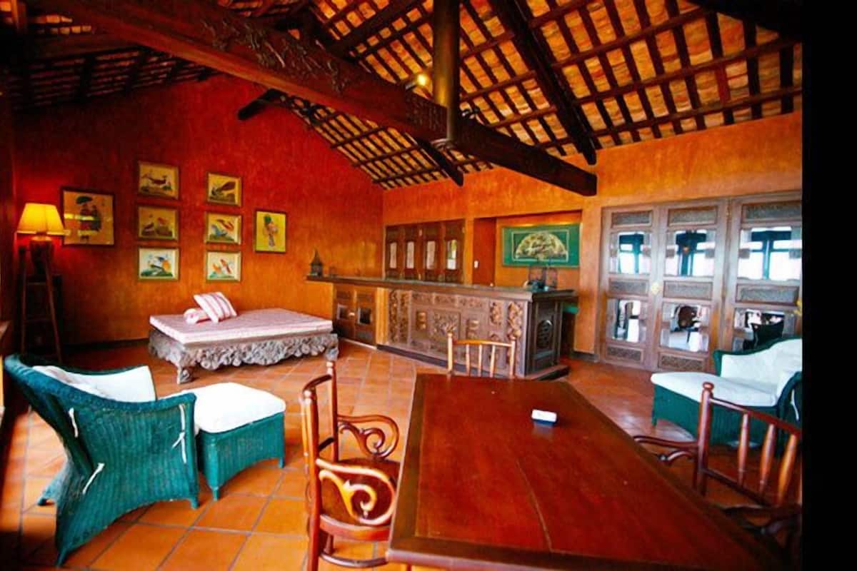 Una habitación con techo de madera, una camilla de masaje y sillas. Hay cuadros en la pared y una ventana con vistas.